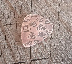 Copper guitar pick with hearts and hammered patterning