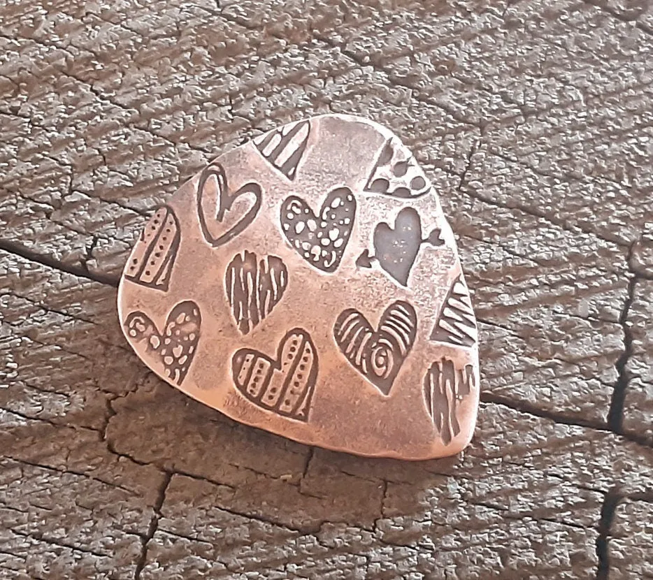 Copper guitar pick with hearts and hammered patterning